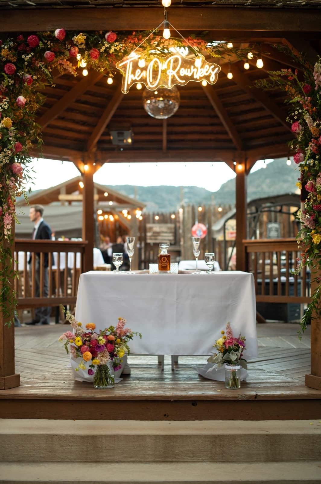 Sweetheart table with custom neon sign, gazebo, floral arch, and string lights